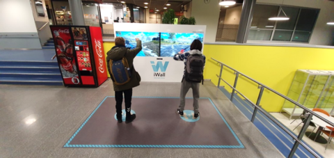 Kaksi ihmistä pelaamassa digitaalisen seinänäytön edessä.