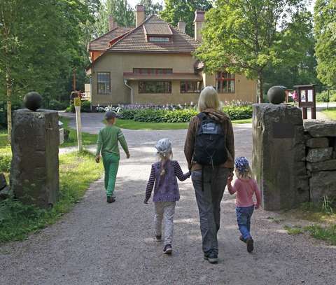 Aikuinen ja kolme lasta menossa Villa Elfvikin luontotaloon aurinkoisena kesäpäivänä.