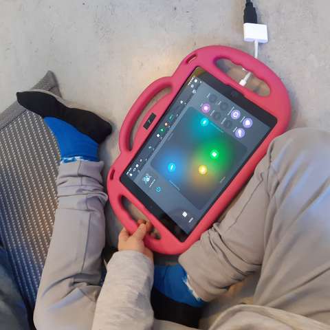 •	A child holds a virtual smart instrument in their lap. A smart instrument is an application used on a tablet device.