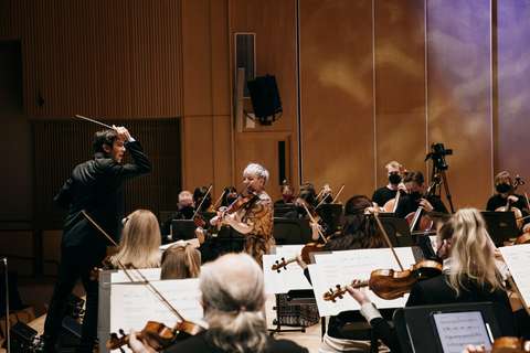 Kapellimestari, viulua soittava solisti sekä orkesterin soittajia lavalla.