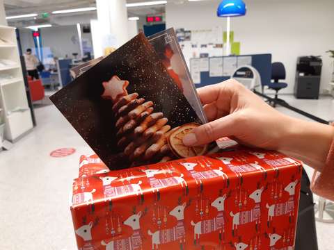 Käsi pudottaa joulukortteja laatikkoon, joka on koristeltu joulupaperilla.