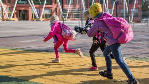 Three pupils running with backpacks in the school yard.